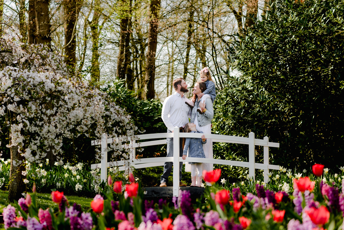 A joyful family shares a tender moment on a white bridge surrounded by blooming tulips, hyacinths, and cherry blossoms in Keukenhof Gardens during an early April spring photo session in the Netherlands.