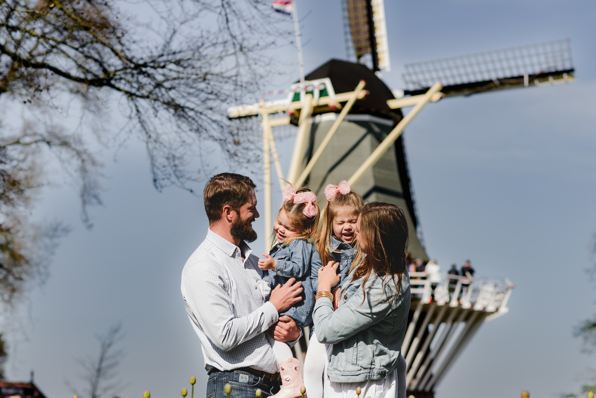 A smiling family stands in front of the famous windmill at Keukenhof Gardens during an early April photoshoot, capturing the essence of springtime in the Netherlands with laughter, tradition, and blooming tulips nearby.