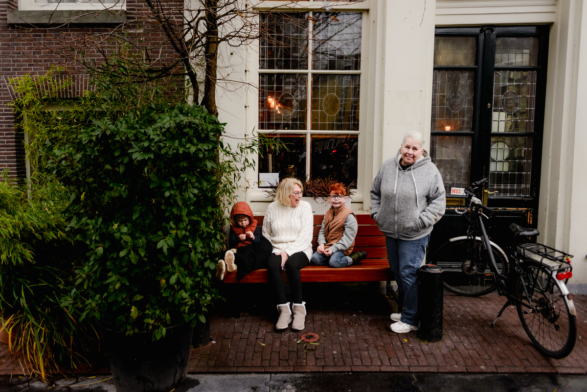 A candid moment of two grandparents and their grandchildren sitting outside a historic Amsterdam home during a December family session—surrounded by greenery, stained glass windows, and parked bikes for an authentic Dutch street scene.