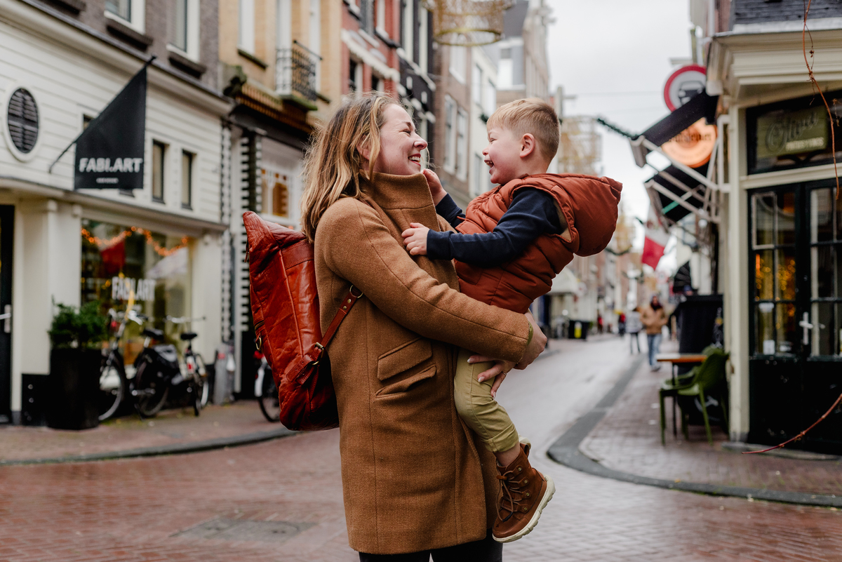 A mother shares a joyful moment with her son on a cobblestone street in Amsterdam’s Nine Streets neighborhood, capturing a warm family connection during a December photo session in the city.
