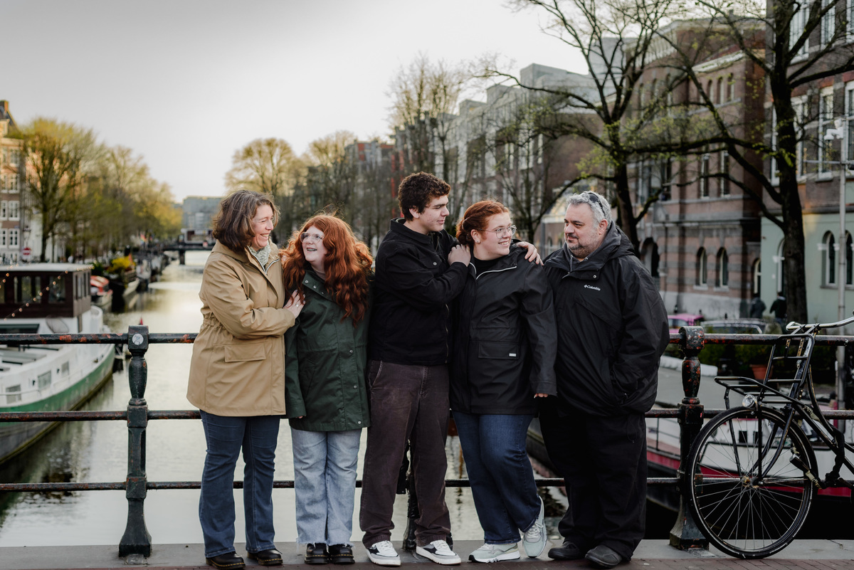 Family standing closely together on a bridge over the canal, sharing a joyful moment with soft morning light and water reflections in the background.