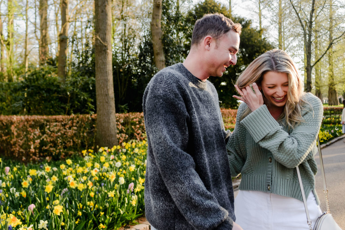 Newly engaged couple laughing and sharing a joyful moment amid yellow daffodils in Keukenhof Gardens.