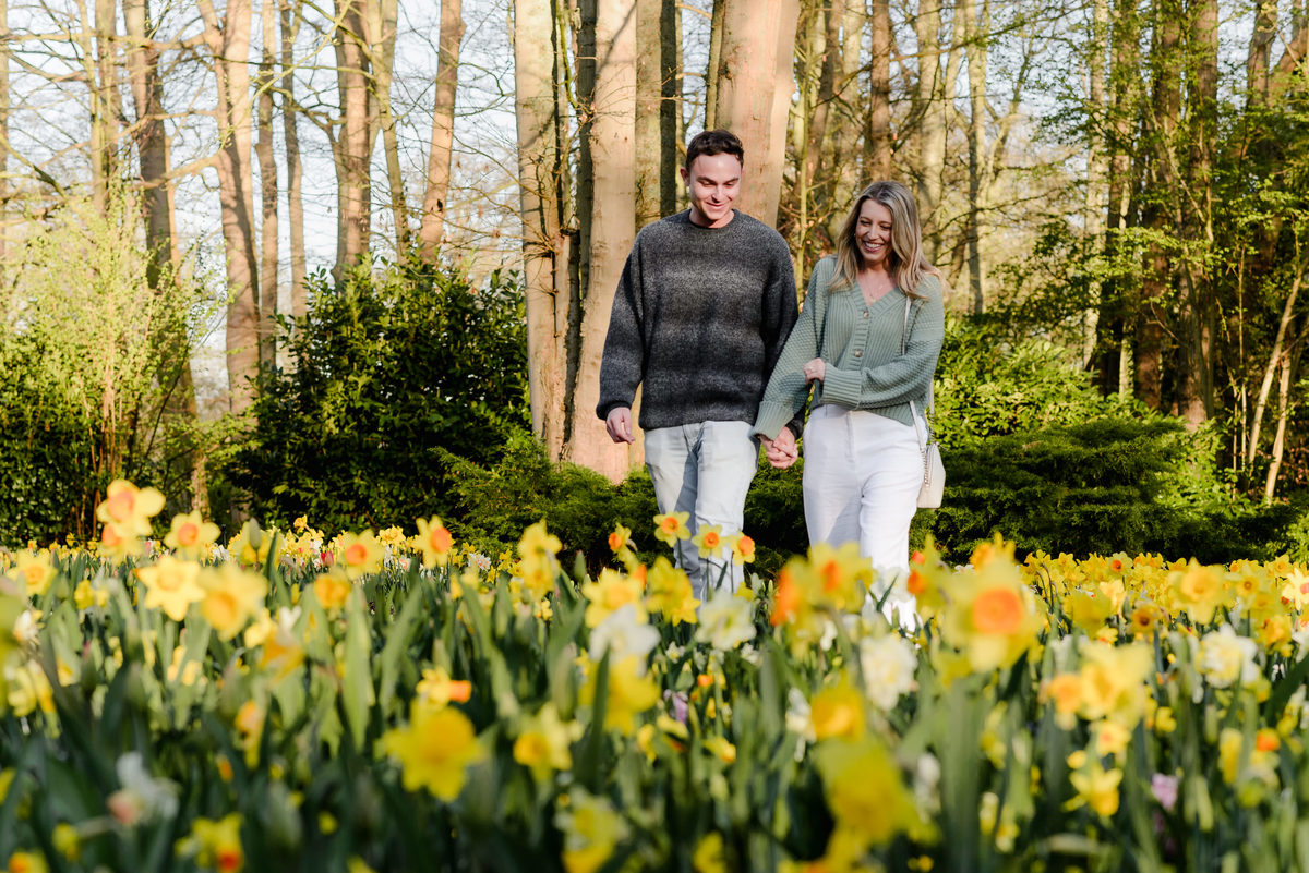 The couple strolls hand-in-hand through a vibrant flower field, beaming with joy after the surprise proposal.