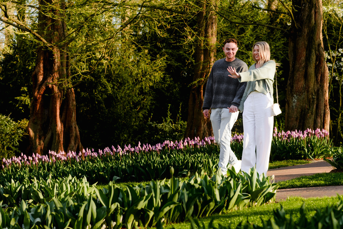 Bride-to-be proudly shows off her engagement ring while walking with her fiancé in a tulip-filled section of Keukenhof.