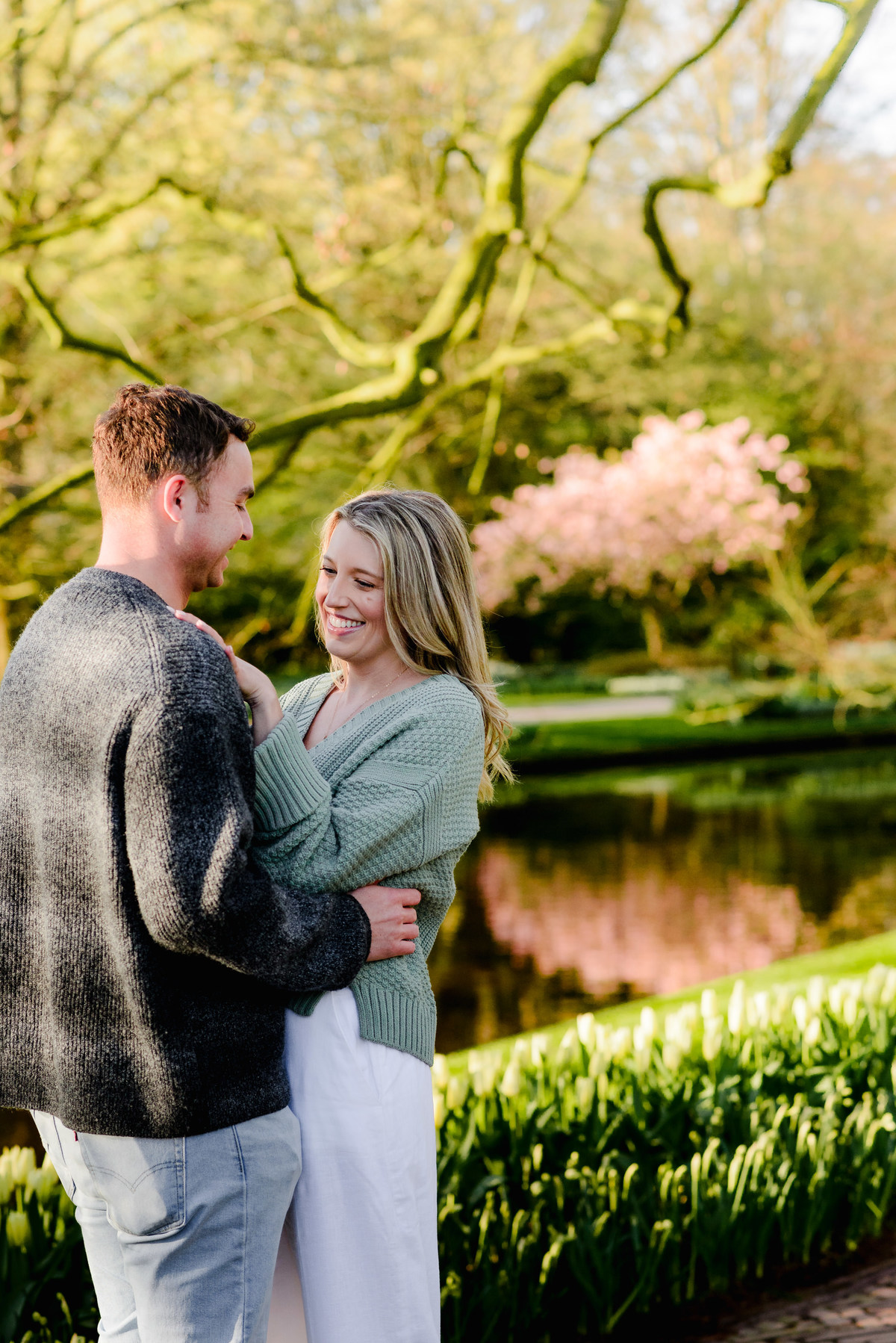 Couple sharing a sweet moment by the water, her hand on his chest and joyful smiles glowing in the golden light.