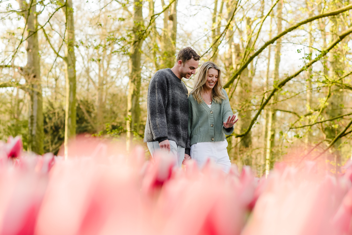 Playful and candid moment of the couple laughing while walking together past a sea of pink tulips.
