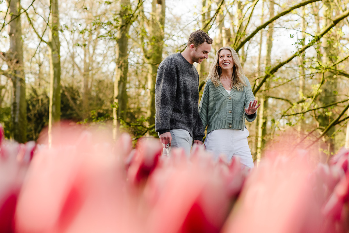 Engaged couple walking hand-in-hand through pink tulip fields, glowing with love in the soft morning light.