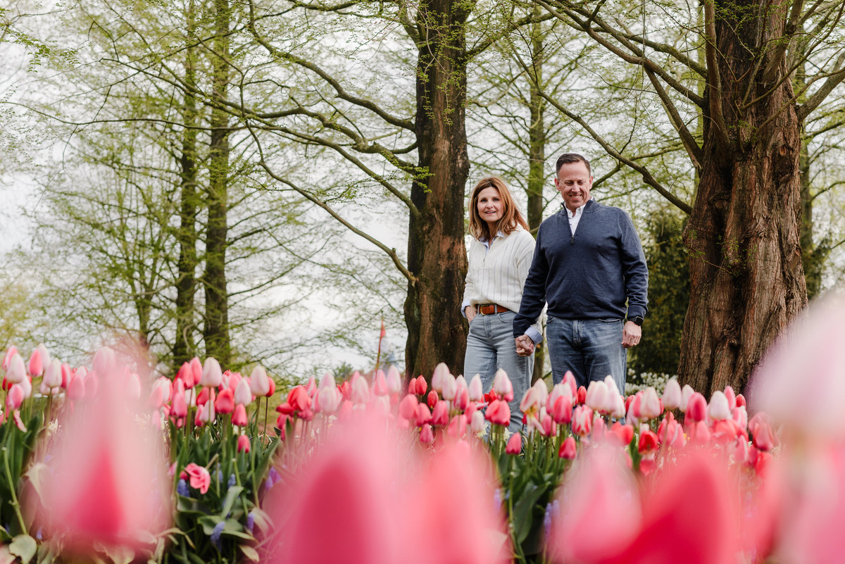 Embracing among blooming pink tulips, the couple shares a joyful moment under Keukenhof’s towering trees and spring canopy.