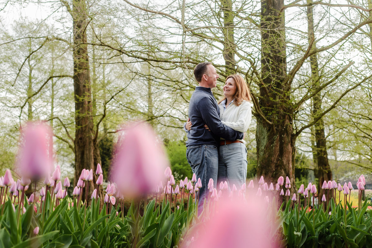 Surrounded by blurred pink tulips in the foreground, the couple exchanges loving smiles beneath Keukenhof's spring canopy.