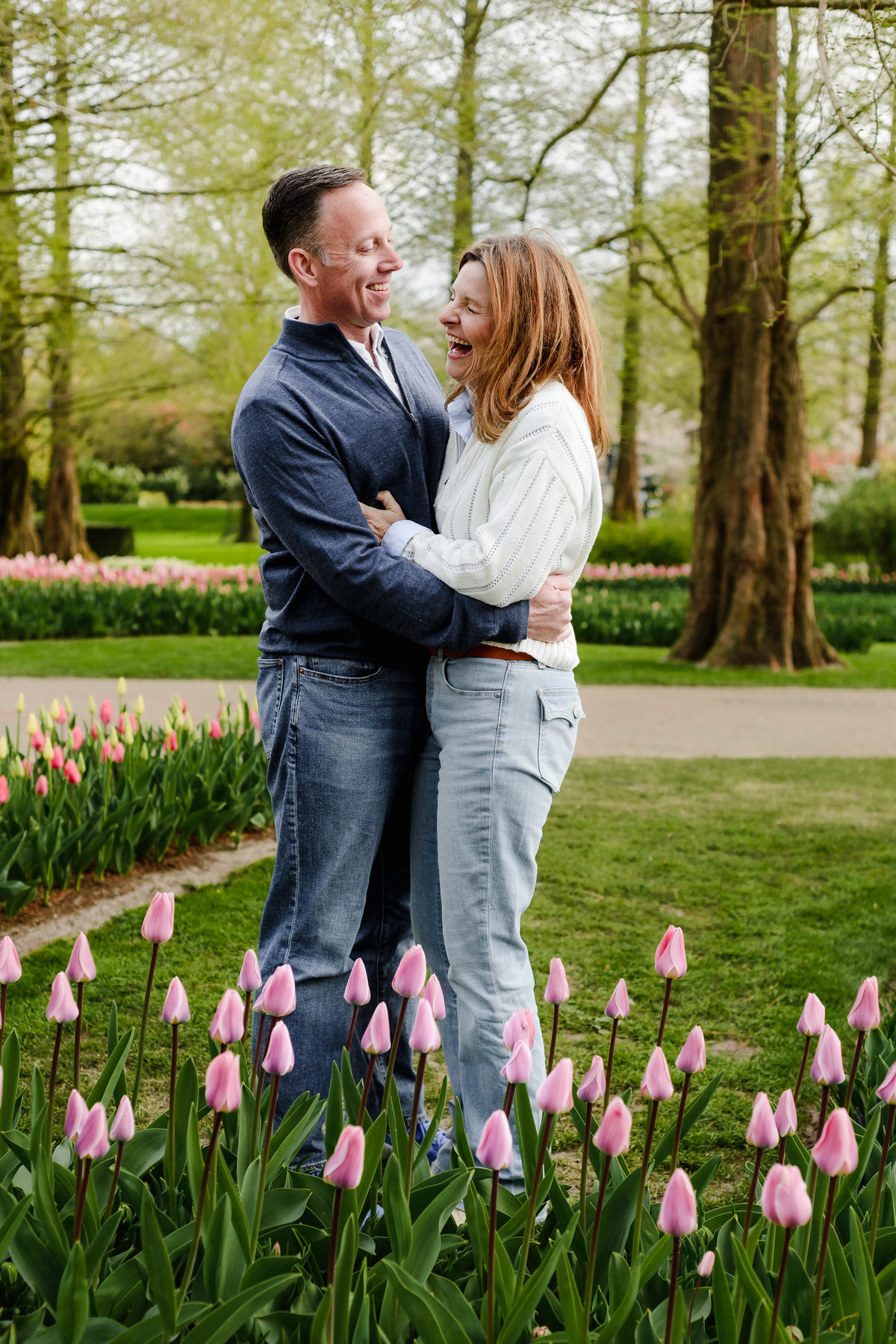 A close-up of the couple laughing and holding each other among freshly budding tulips in a lush spring garden.