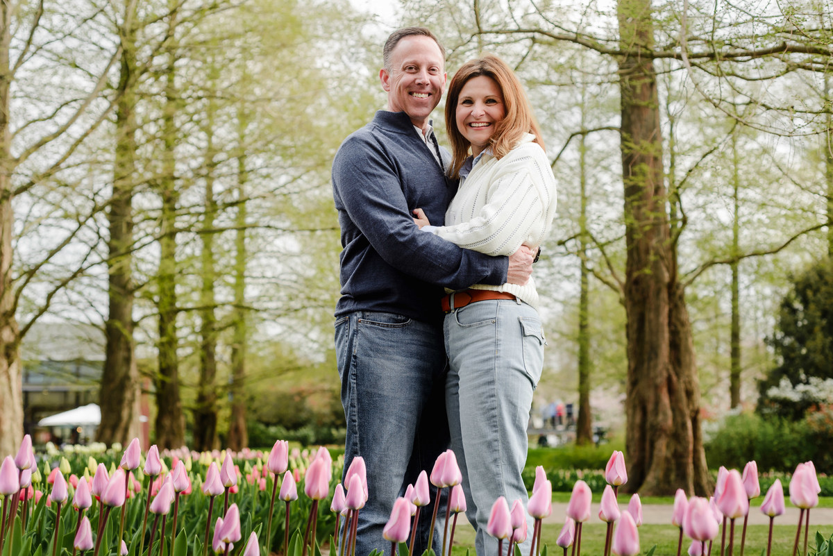 Embracing in a vibrant tulip bed, the couple looks into the camera with warm expressions and soft natural lighting.