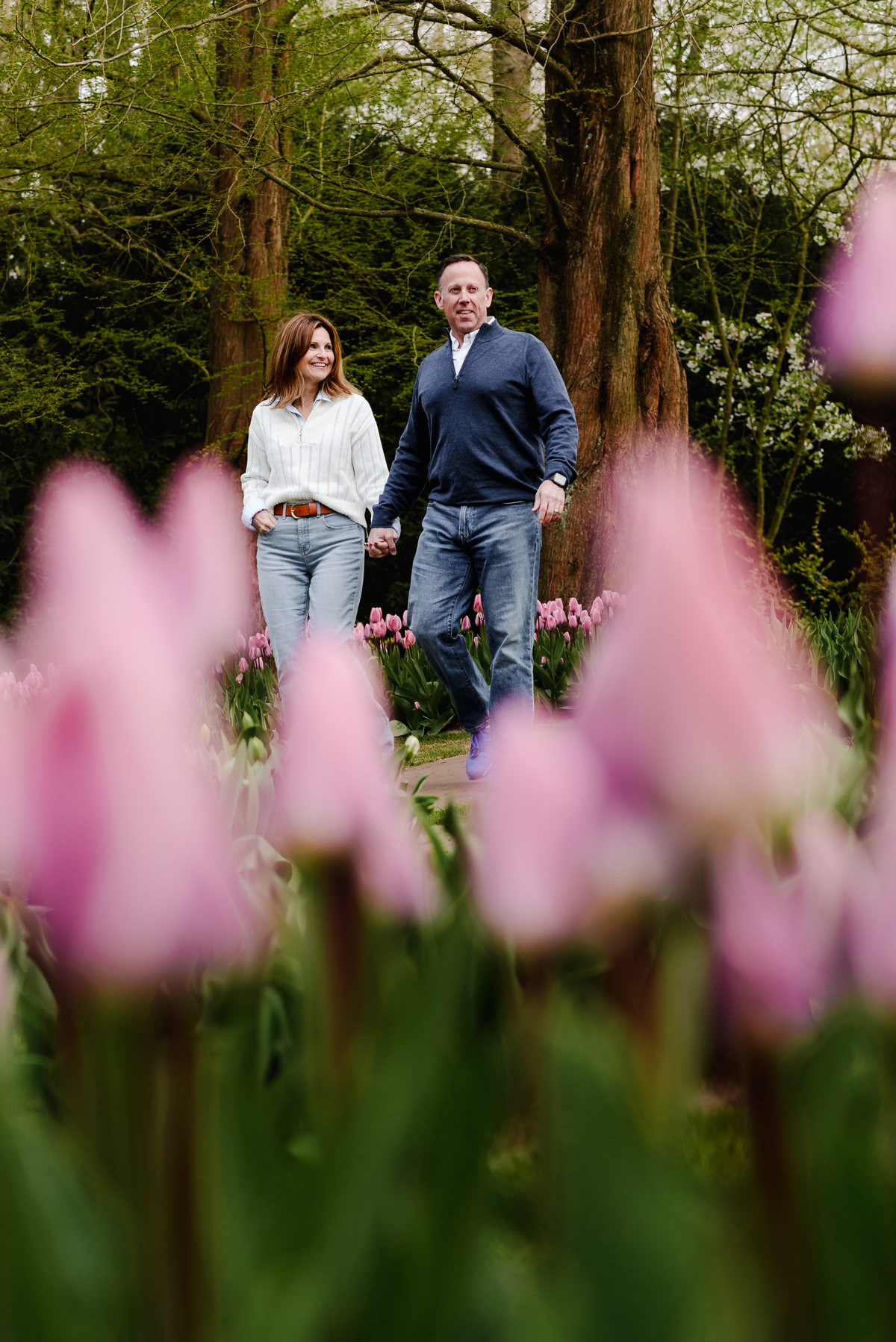 The couple strolls confidently through a blooming garden path, surrounded by vibrant tulips and lush woodland at Keukenhof.