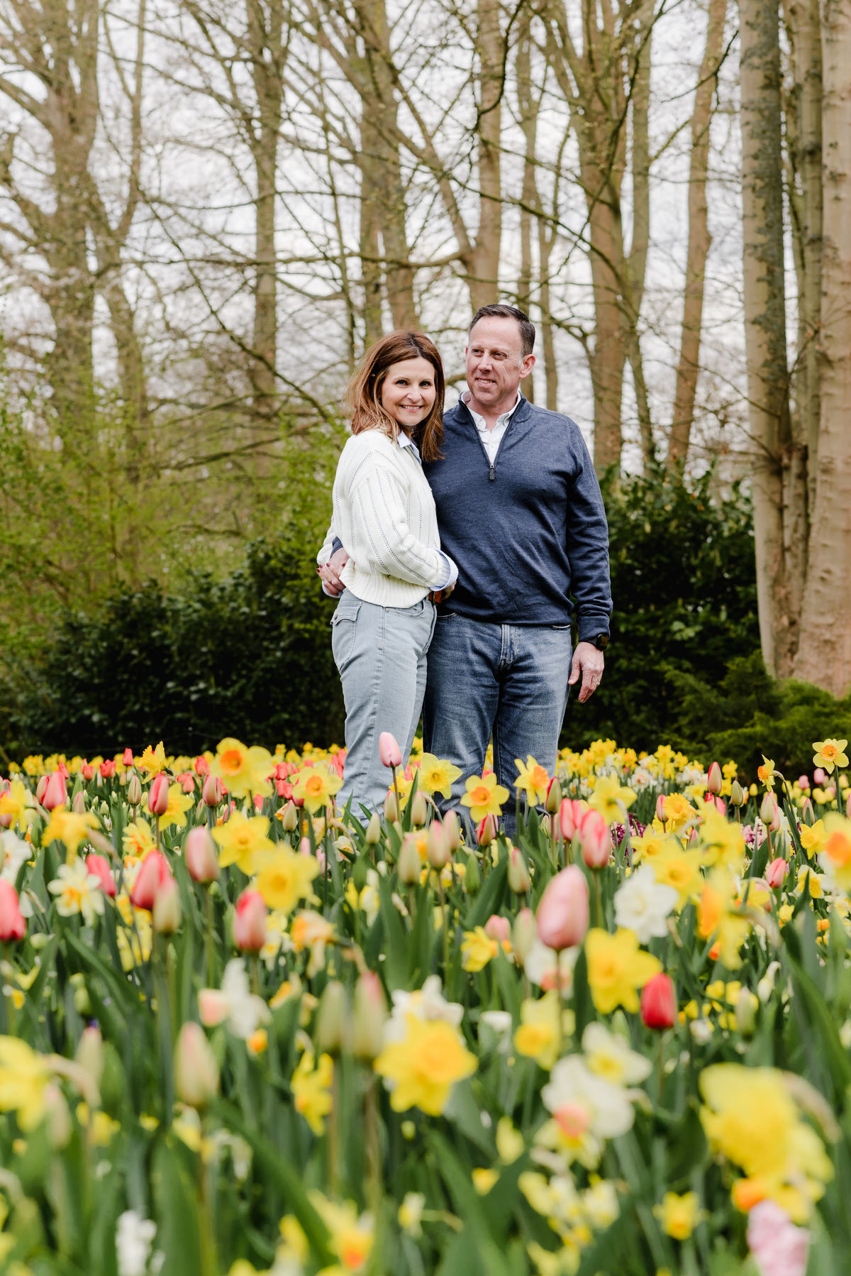 The couple stands side by side among a colorful floral sea, smiling tenderly with pastel tulips and daffodils surrounding them.