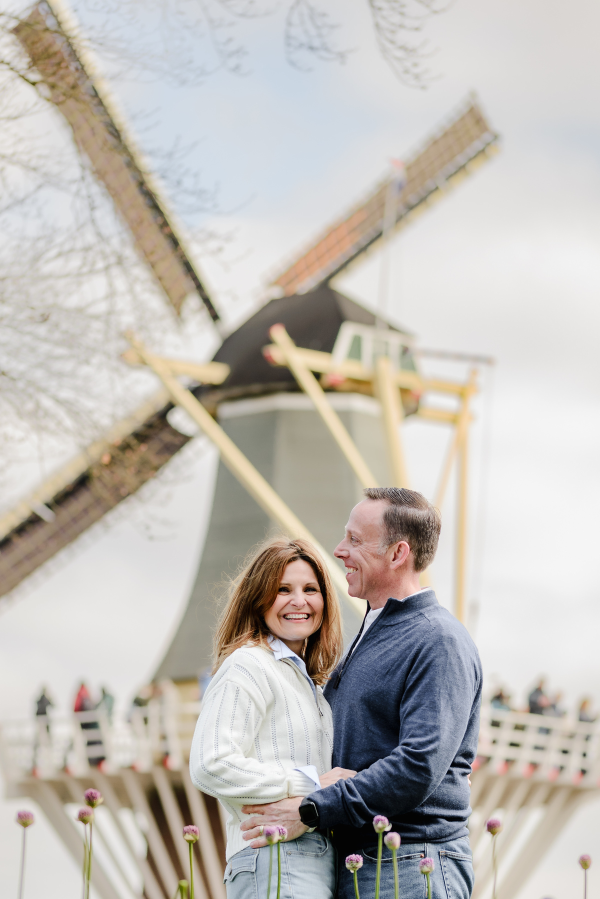 Close-up of a happy couple embracing in front of a traditional windmill, enjoying a bright spring day.