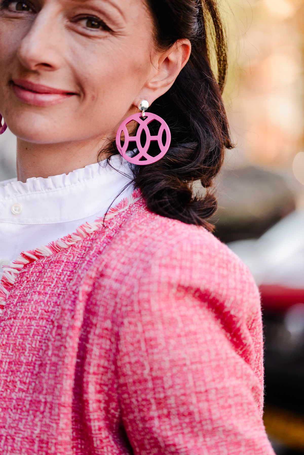 Close-up of woman's face showing vivid pink statement earrings paired with a textured pink jacket.