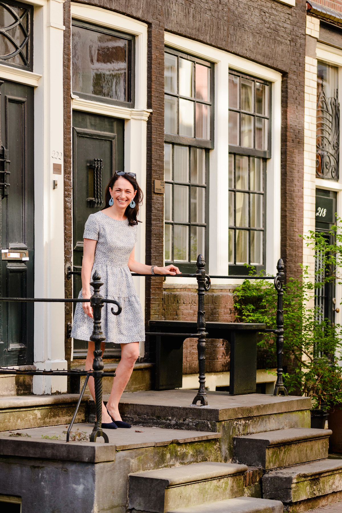 Woman descending stairs outside a historic Amsterdam home, dressed in a short patterned dress and blue earrings.