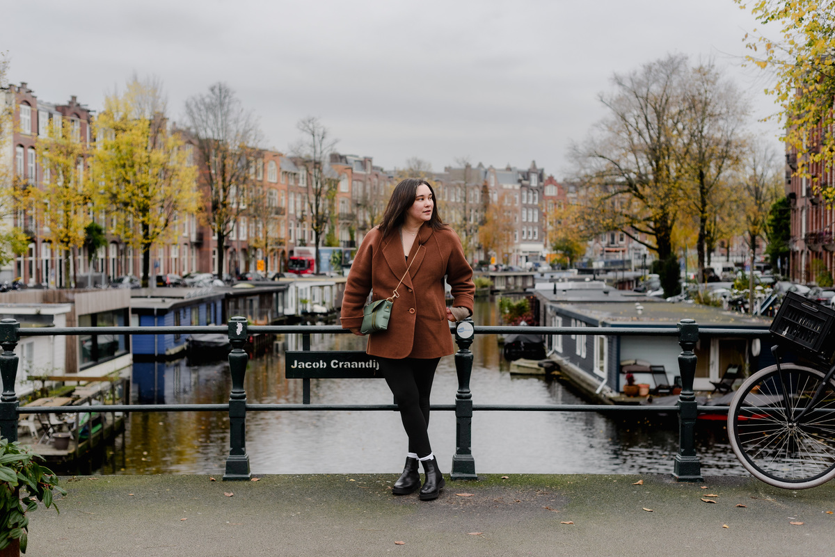 Woman posing casually on a bridge rail in Amsterdam, surrounded by canals and yellowing trees