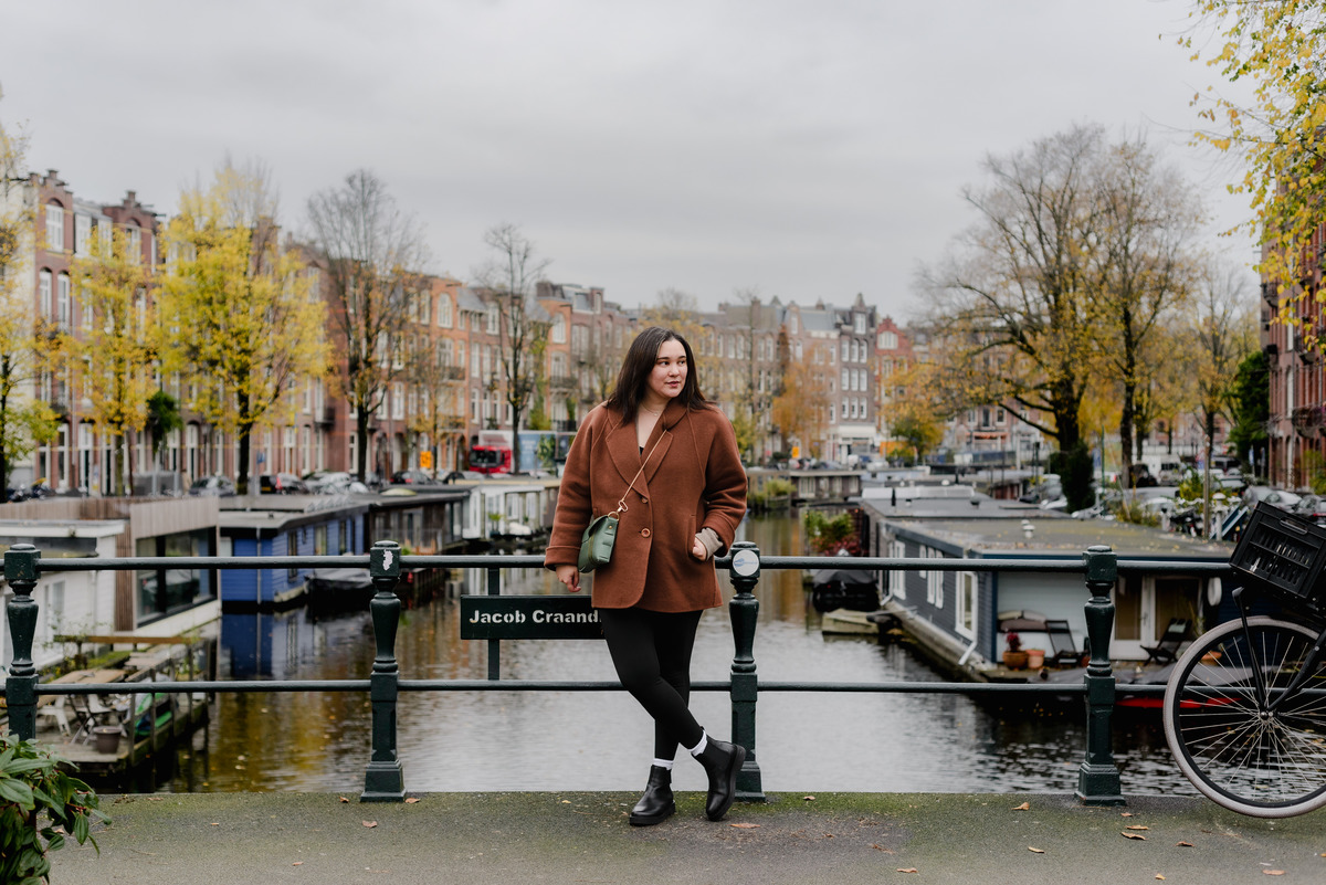 Flash session portrait of a woman in a warm coat, looking to the side with historic Amsterdam homes in the backdrop.