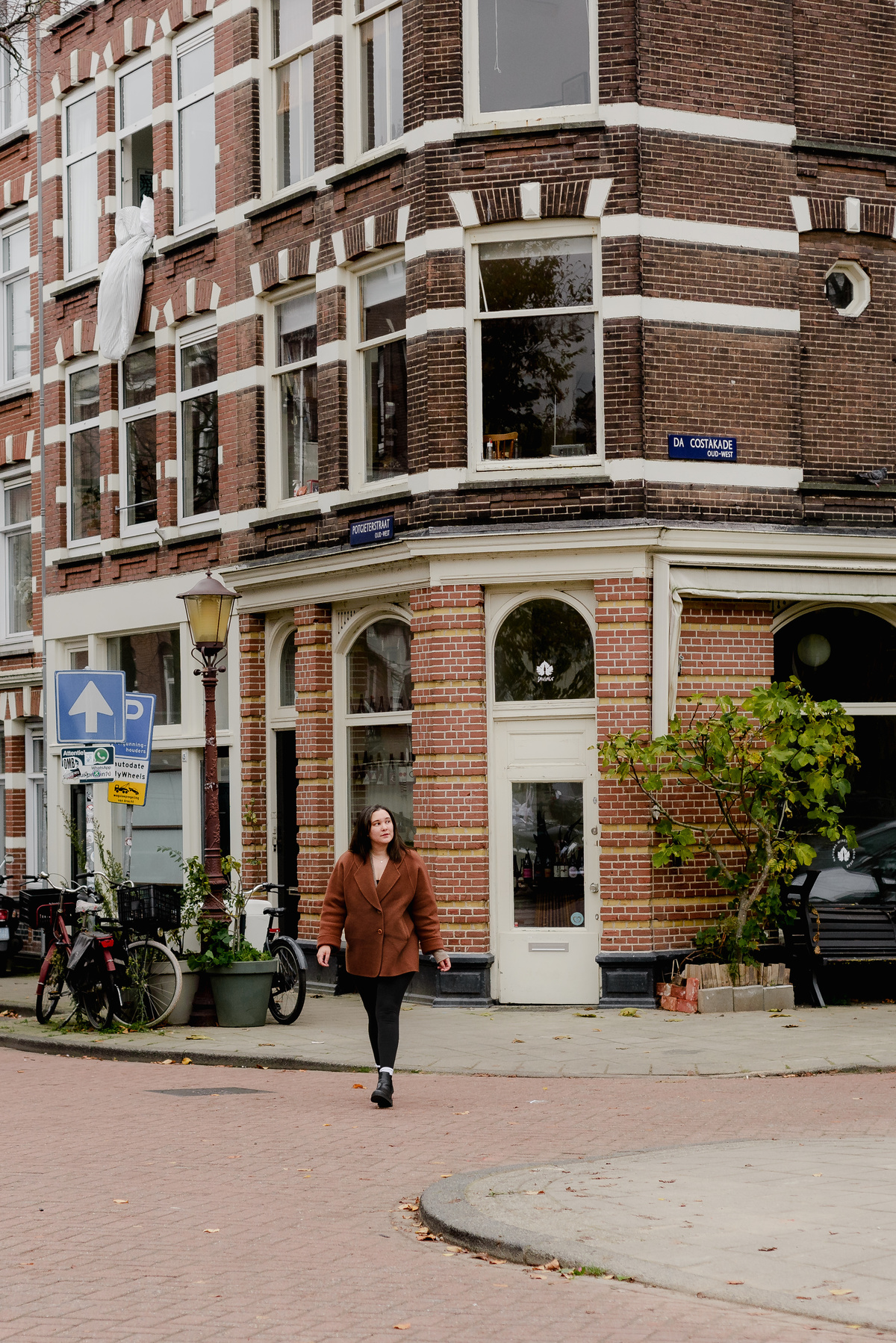 Full-body shot of a woman walking past a historic red brick building on Da Costakade in Amsterdam's Oud West.