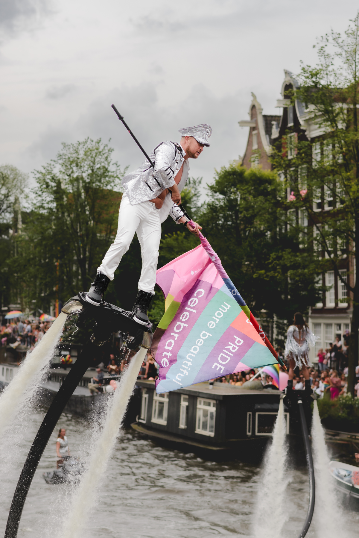 Performer dancing on a decorated Pride boat approaching Prinsengracht, with rainbow details and crowds in the background.