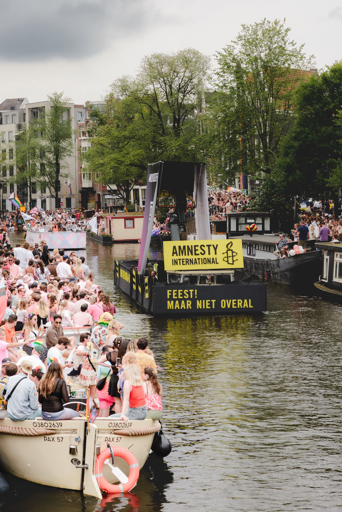 Amnesty International boat with bold yellow signage reading “Feest! Maar niet overal” (Party! But not everywhere) moving through the Pride Canal Parade.