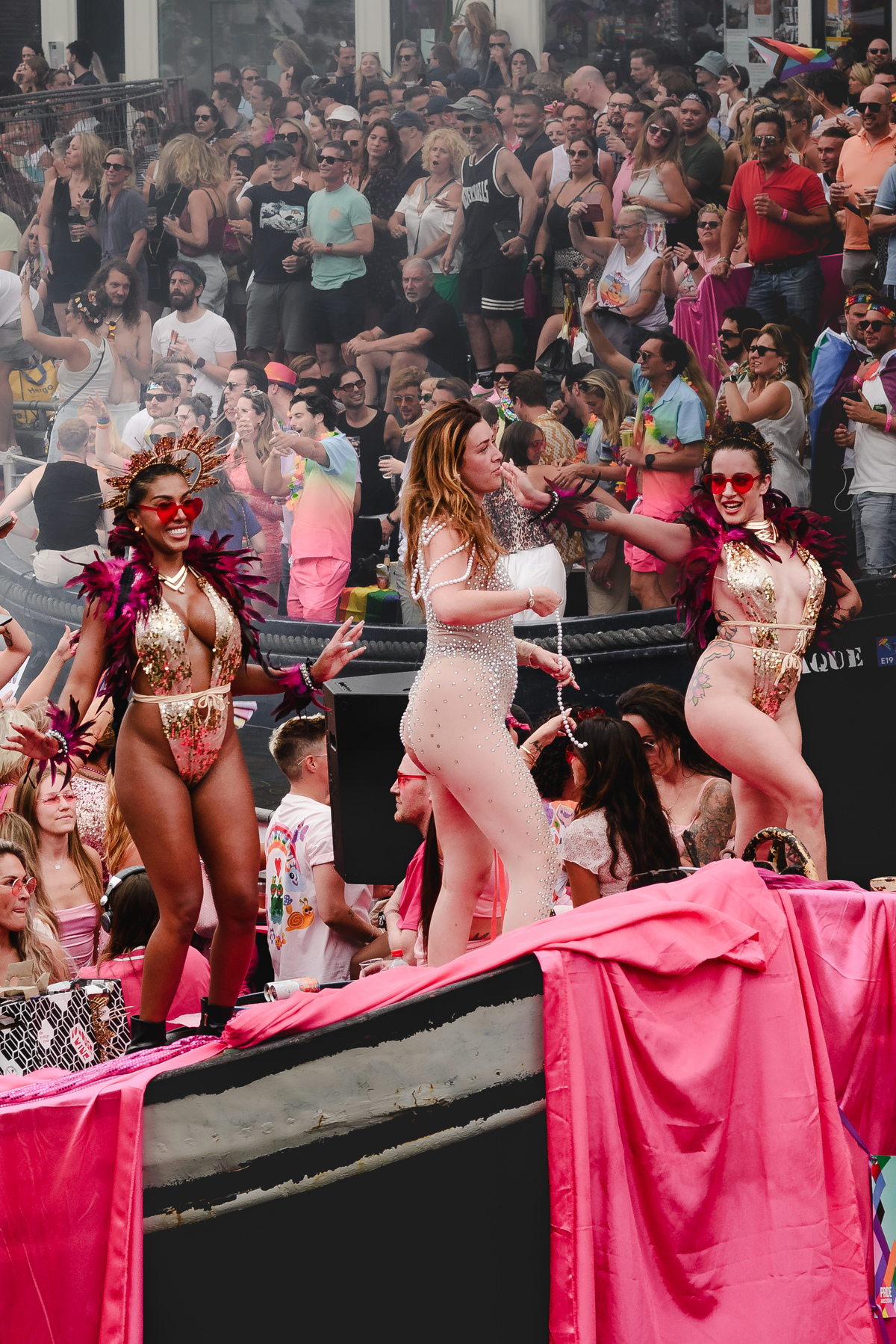 Close-up of a performer waving a rainbow flag with joy, framed by the canal and historic buildings.