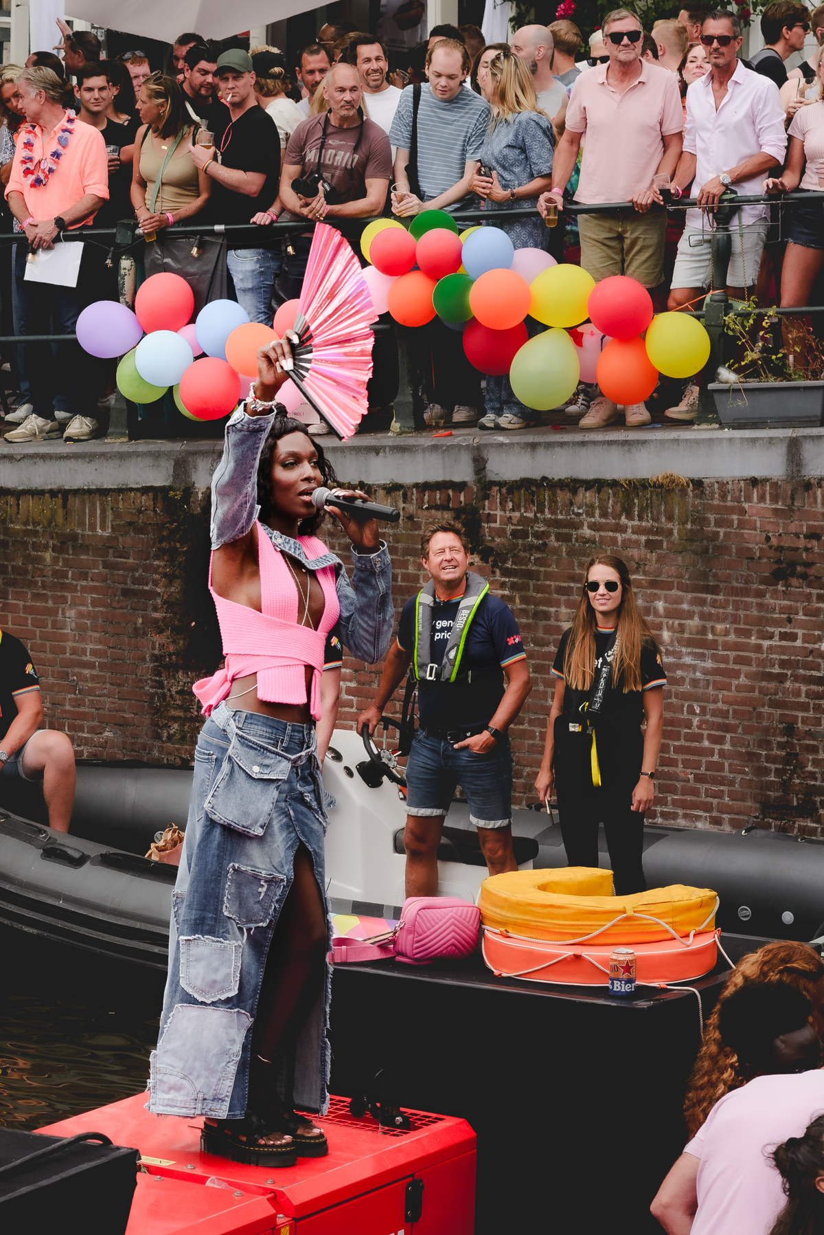 Two dancers on a Pride boat mid-performance, surrounded by vibrant decorations and cheering crowds.
