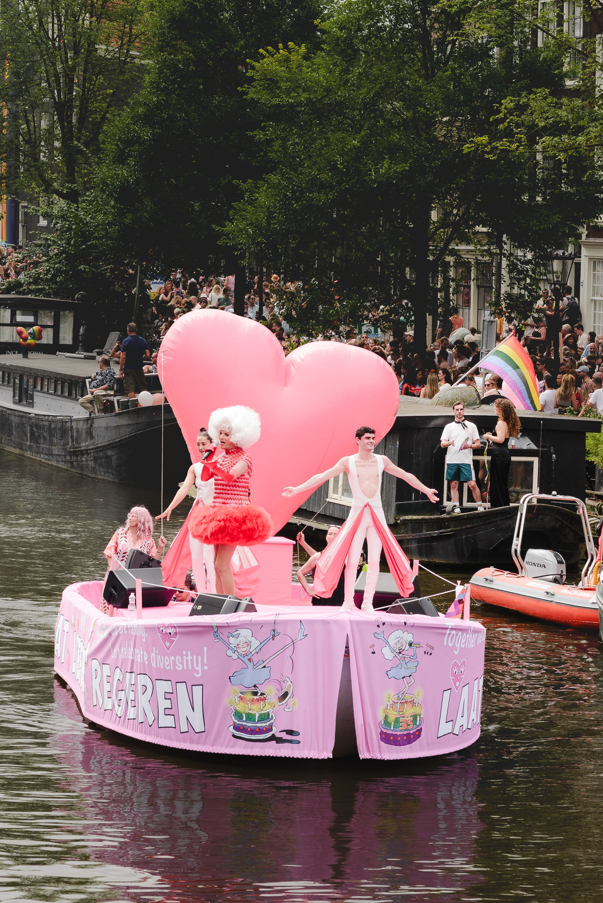 Two dancers on a Pride boat mid-performance, surrounded by vibrant decorations and cheering crowds.