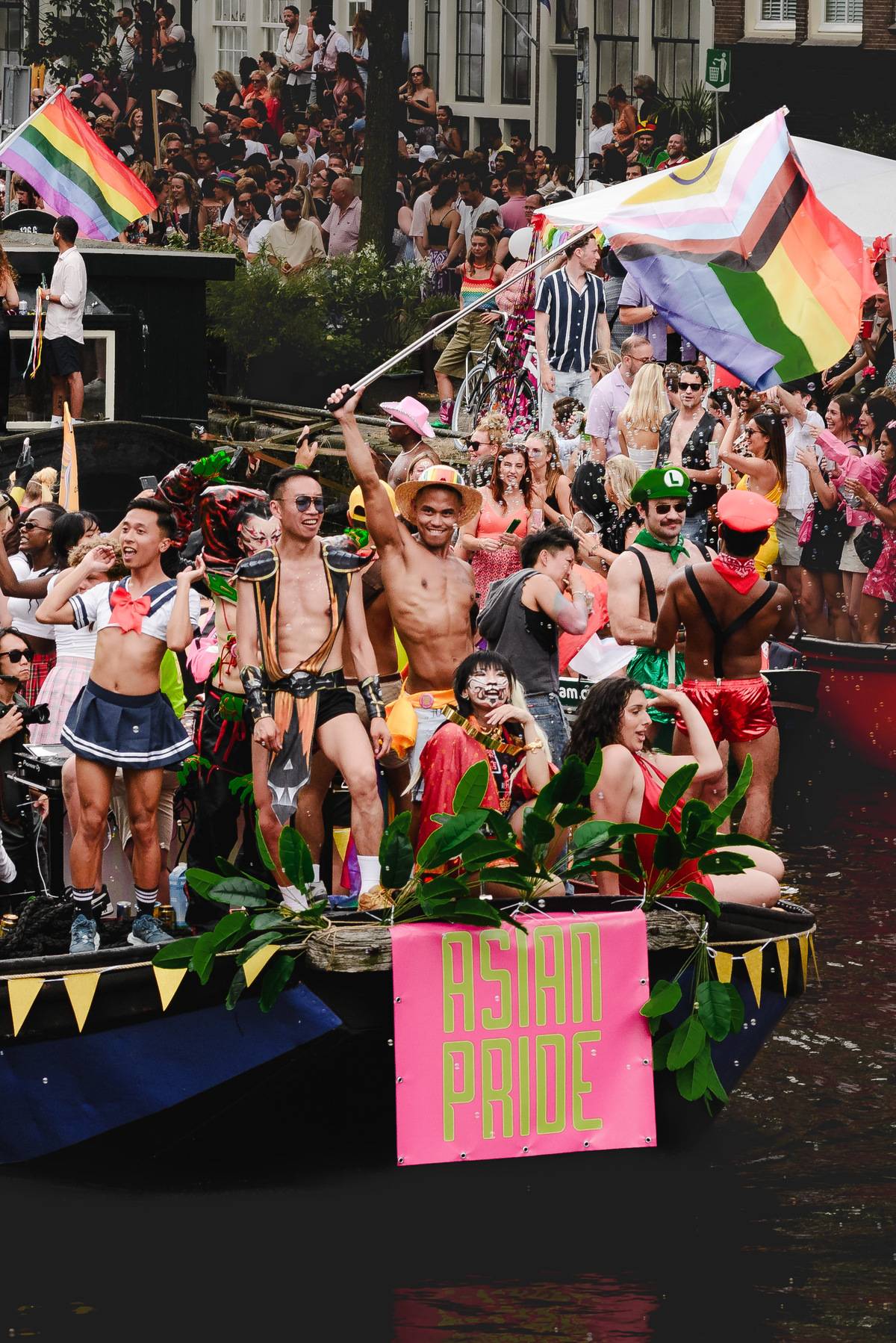Boat entering frame on the canal, surrounded by people lining the bridges and edges of Prinsengracht.