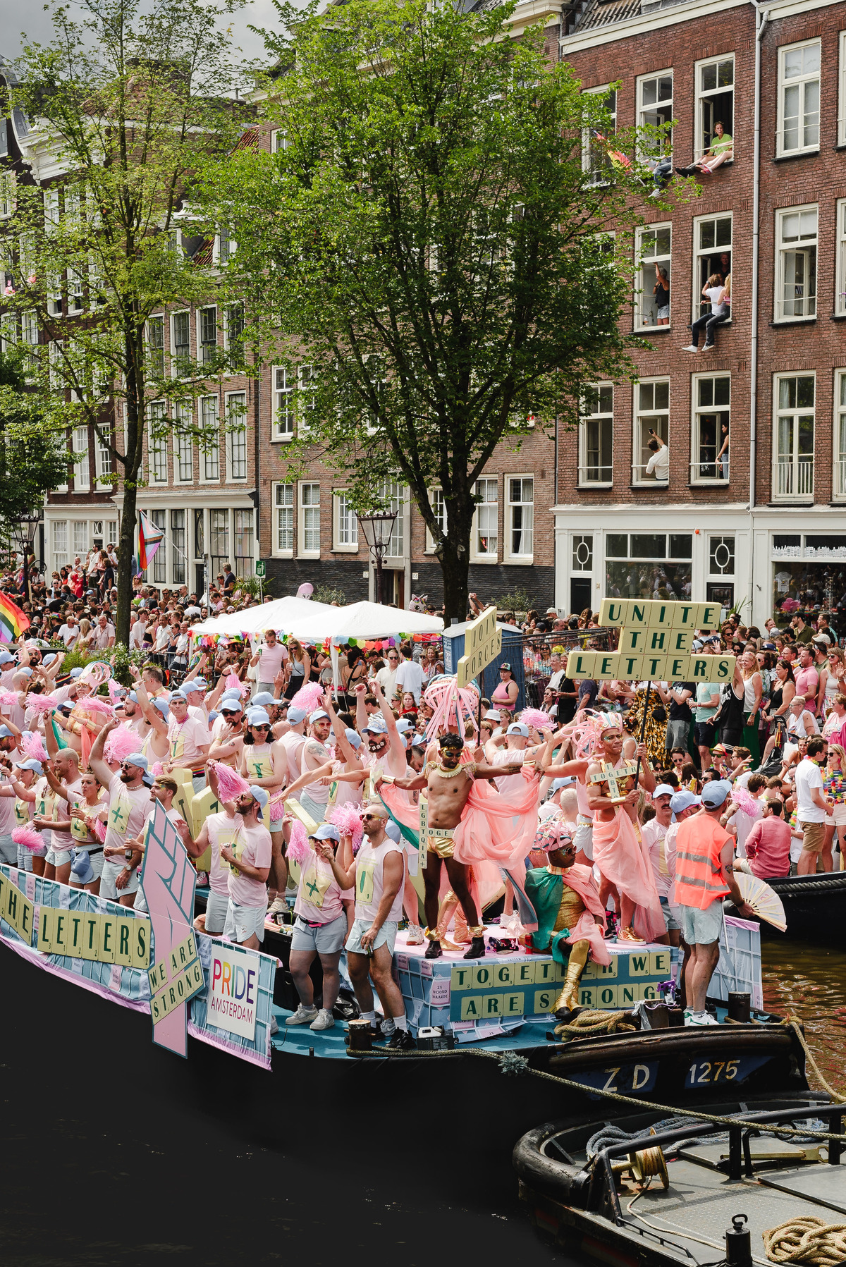 Performers dancing enthusiastically as the boat crosses under a bridge, with festive atmosphere around.