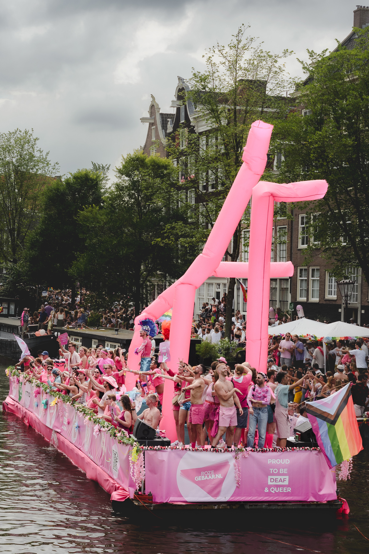 Performers dancing enthusiastically as the boat crosses under a bridge, with festive atmosphere around.