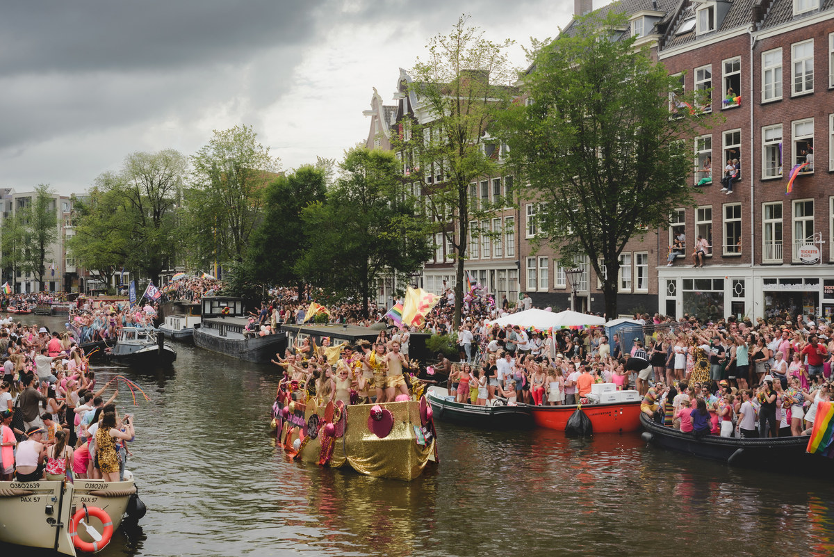 Performers dancing enthusiastically as the boat crosses under a bridge, with festive atmosphere around.