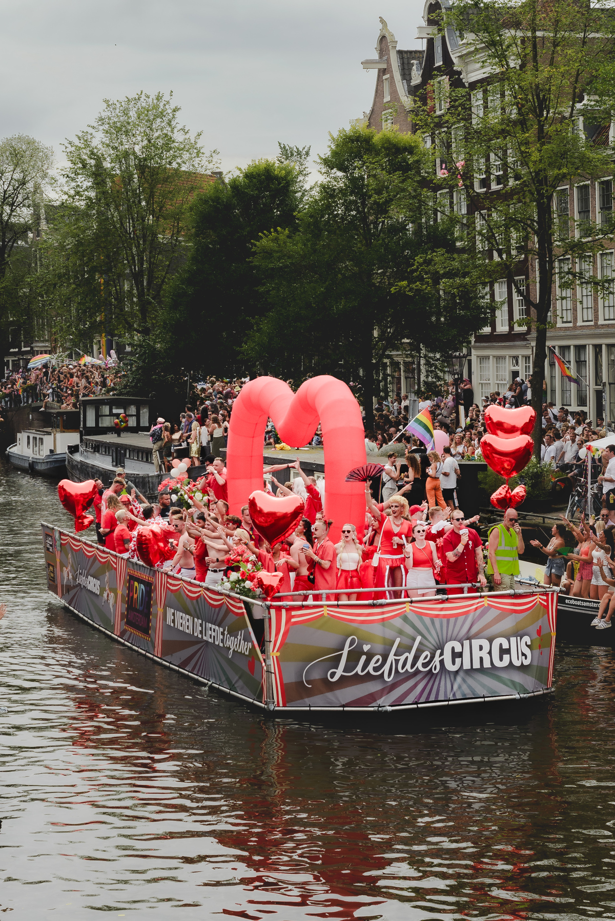 Performers dancing enthusiastically as the boat crosses under a bridge, with festive atmosphere around.