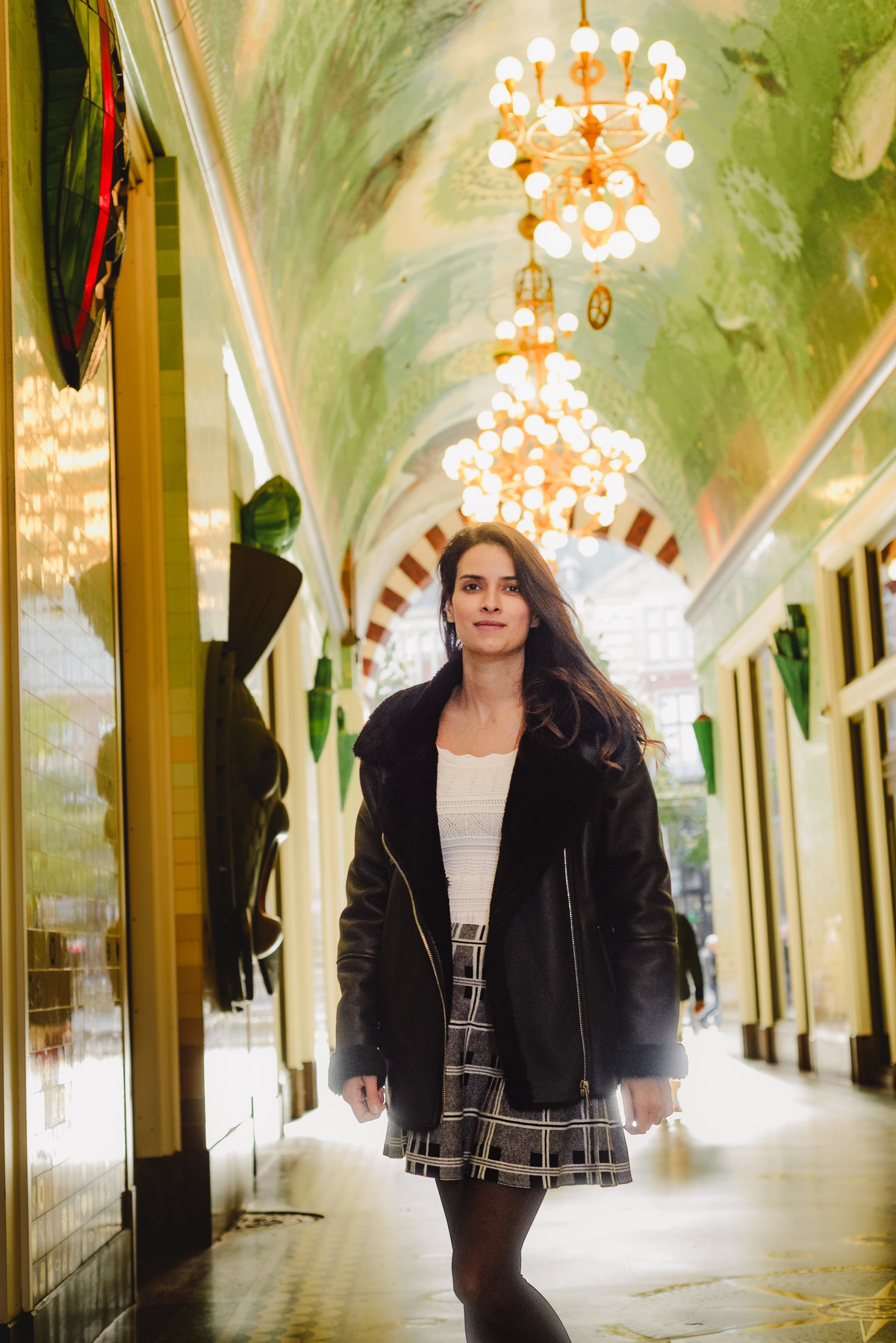 Solo traveler walking through Amsterdam’s Beurspassage, framed by its green mosaic tiles and golden chandeliers during a guided photo session.