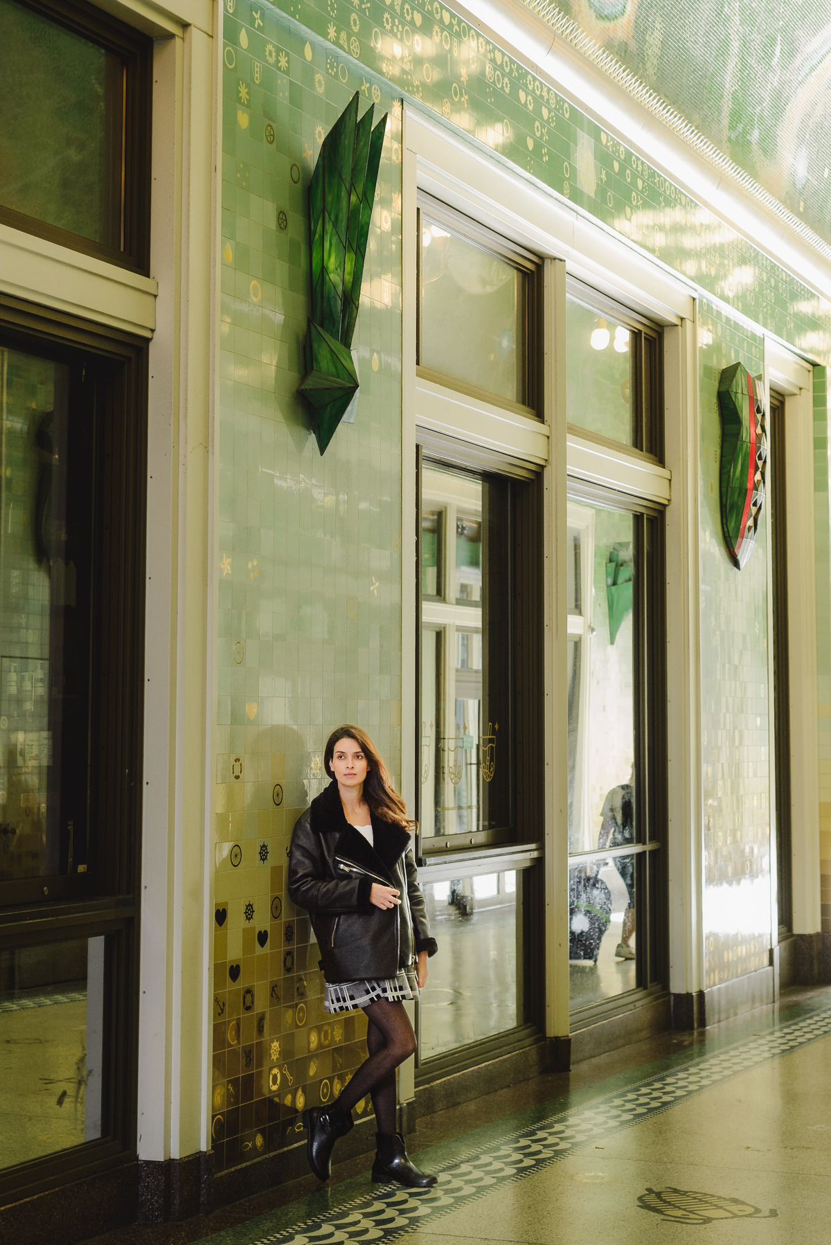 Woman posing inside the Beurspassage in Amsterdam, standing by its decorative green tiles and glass artwork during an Explorer photography tour.