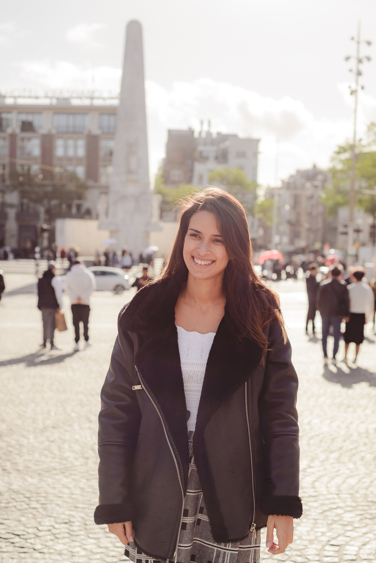 Traveler smiling in Dam Square with the National Monument in the background during a sunny Explorer photo session in Amsterdam.