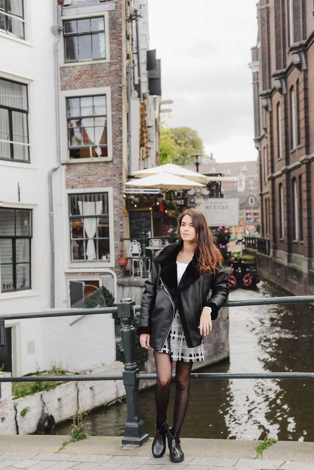 Solo woman posing on a small Amsterdam bridge overlooking a narrow canal and historic homes during a city photography tour.