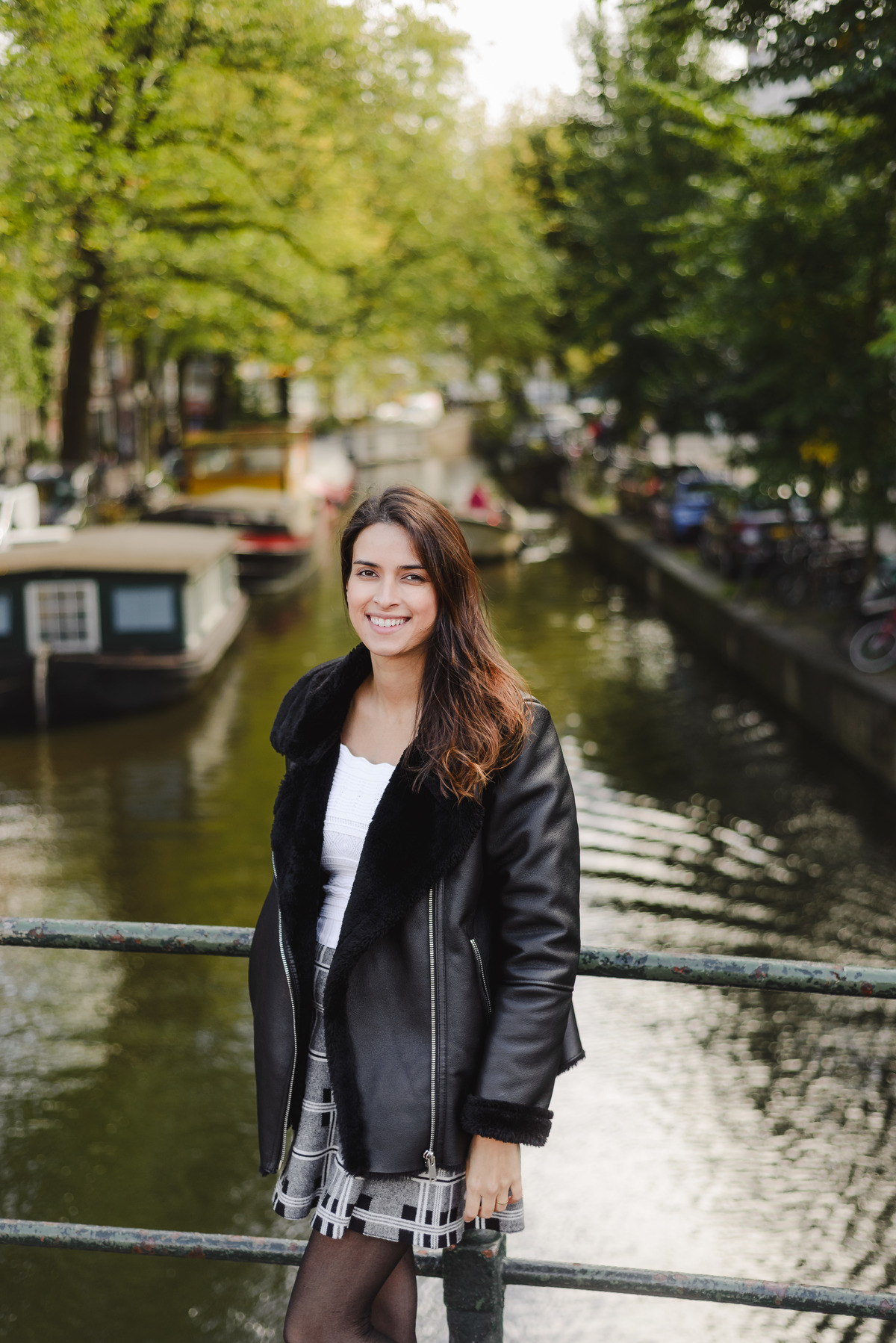 Woman looking down with her hands on her belly while standing on a canal bridge in Amsterdam.