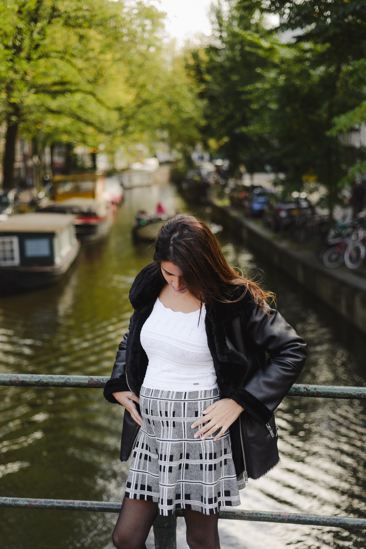 Woman standing on a bridge, holding her belly gently, with houseboats and trees lining the canal.