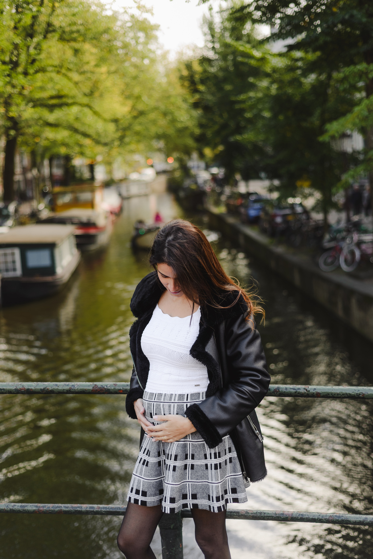 Woman smiling at the camera while standing on a quiet canal bridge, with sunlight reflecting on the water.