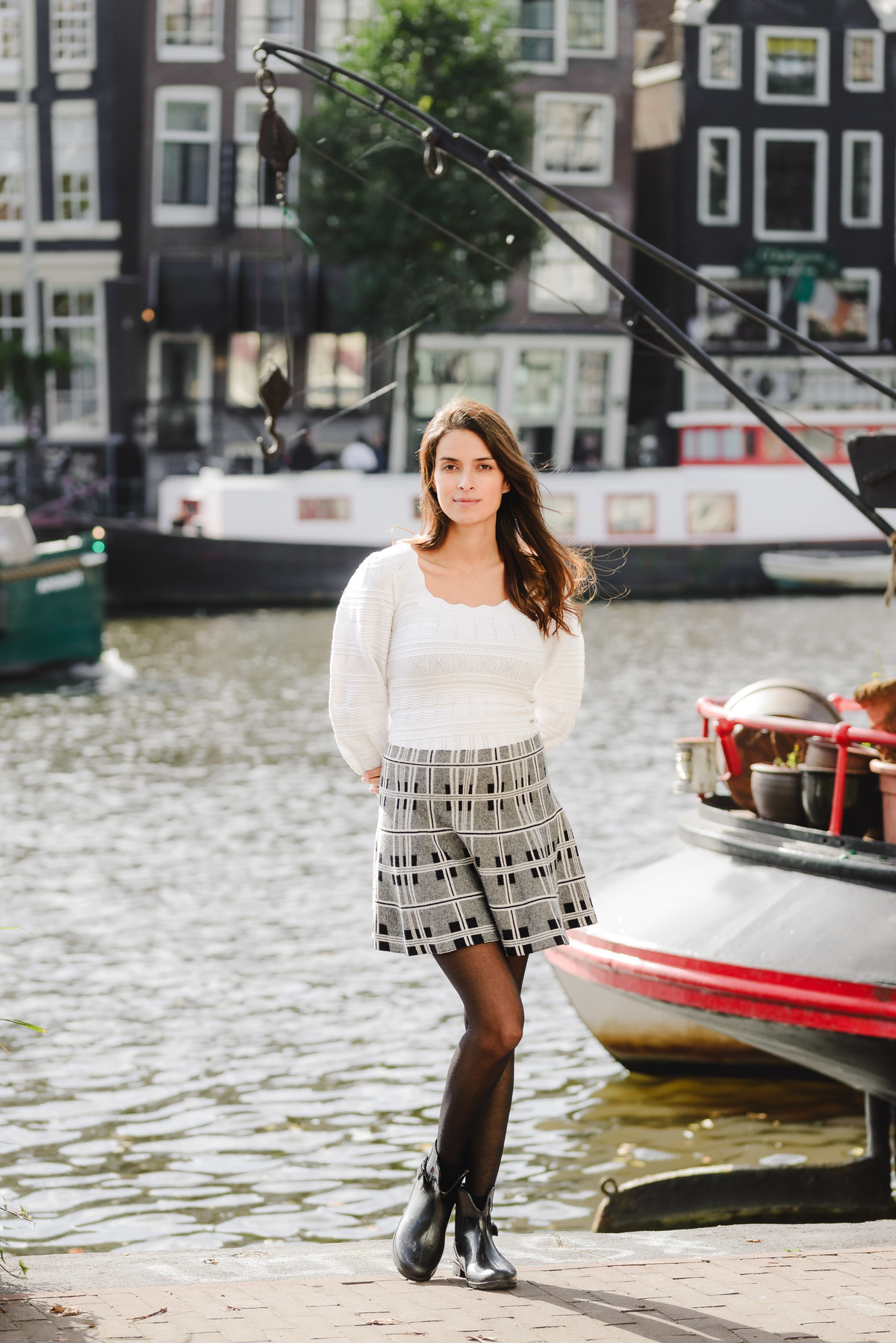 Woman standing by the canal in Amsterdam, framed by boats and tall canal houses.