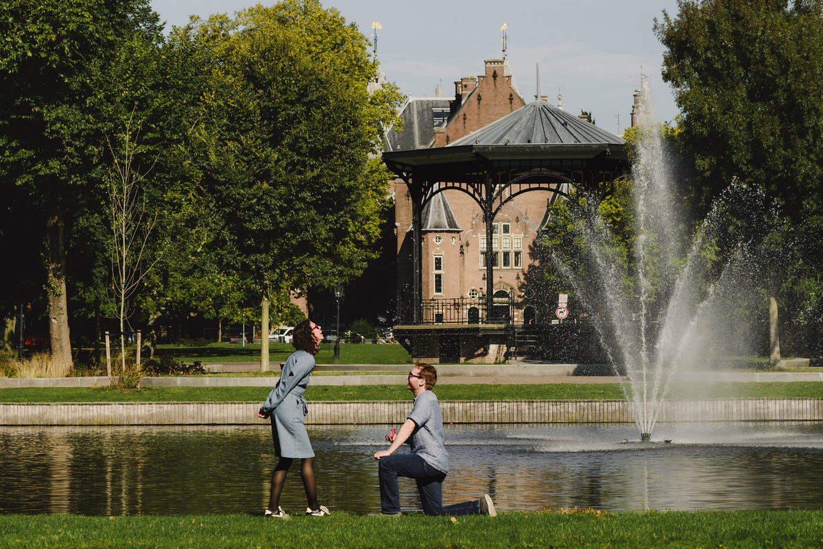 Couple in front of Oosterpark gazebo. Man is proposing on one knee. Surprise engagement proposal in Amsterdam, The Netherlands