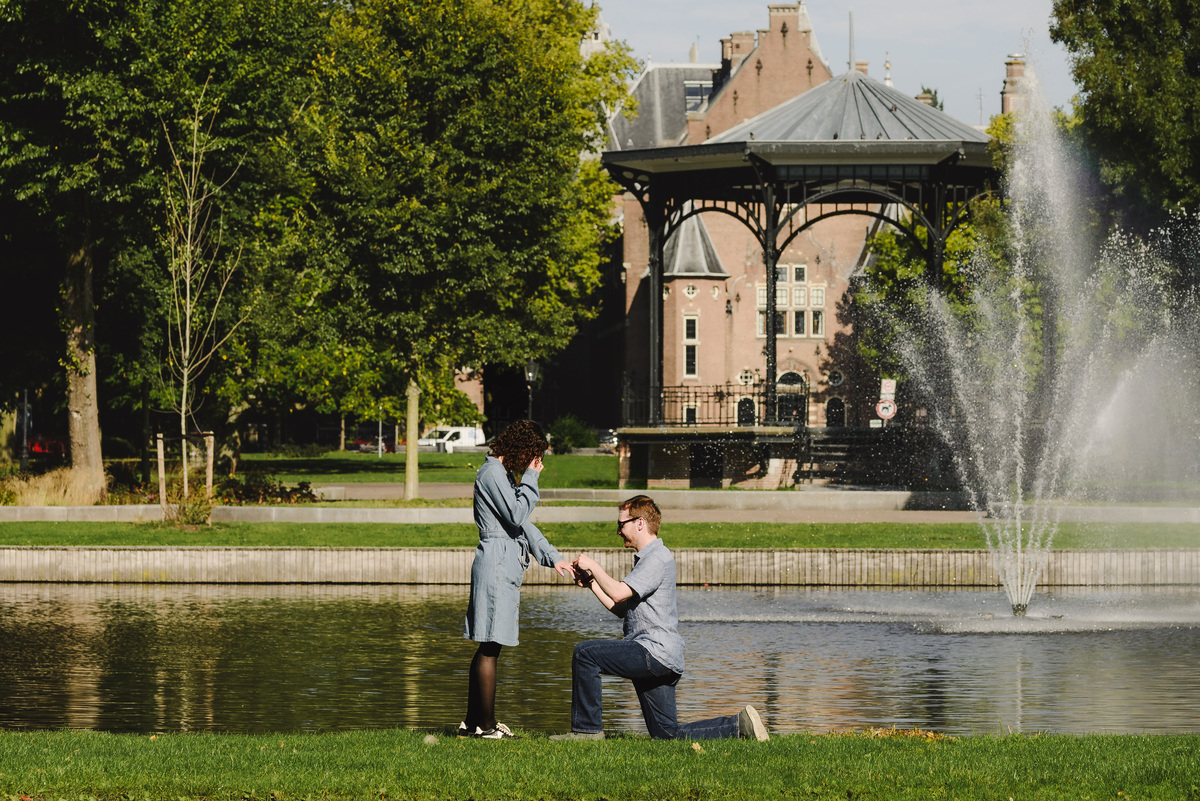 Couple in front of Oosterpark gazebo. Man is proposing on one knee. Surprise engagement proposal in Amsterdam, The Netherlands