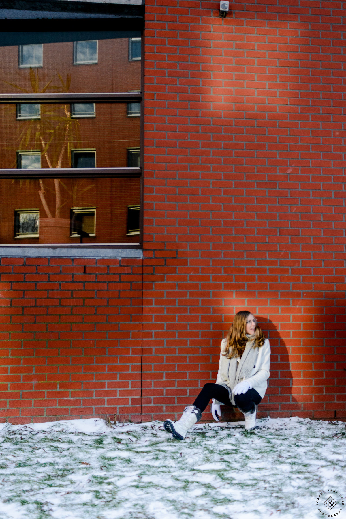 Woman seated against a red brick wall in Amsterdam during winter, surrounded by patches of snow, photographed in natural winter light.