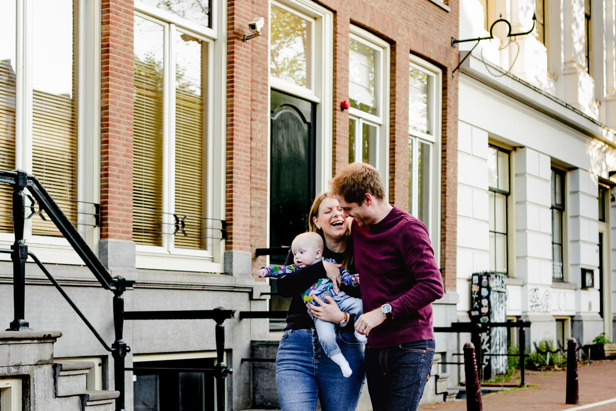 Mother and father laughing together while holding their baby during a family photo session in Amsterdam.