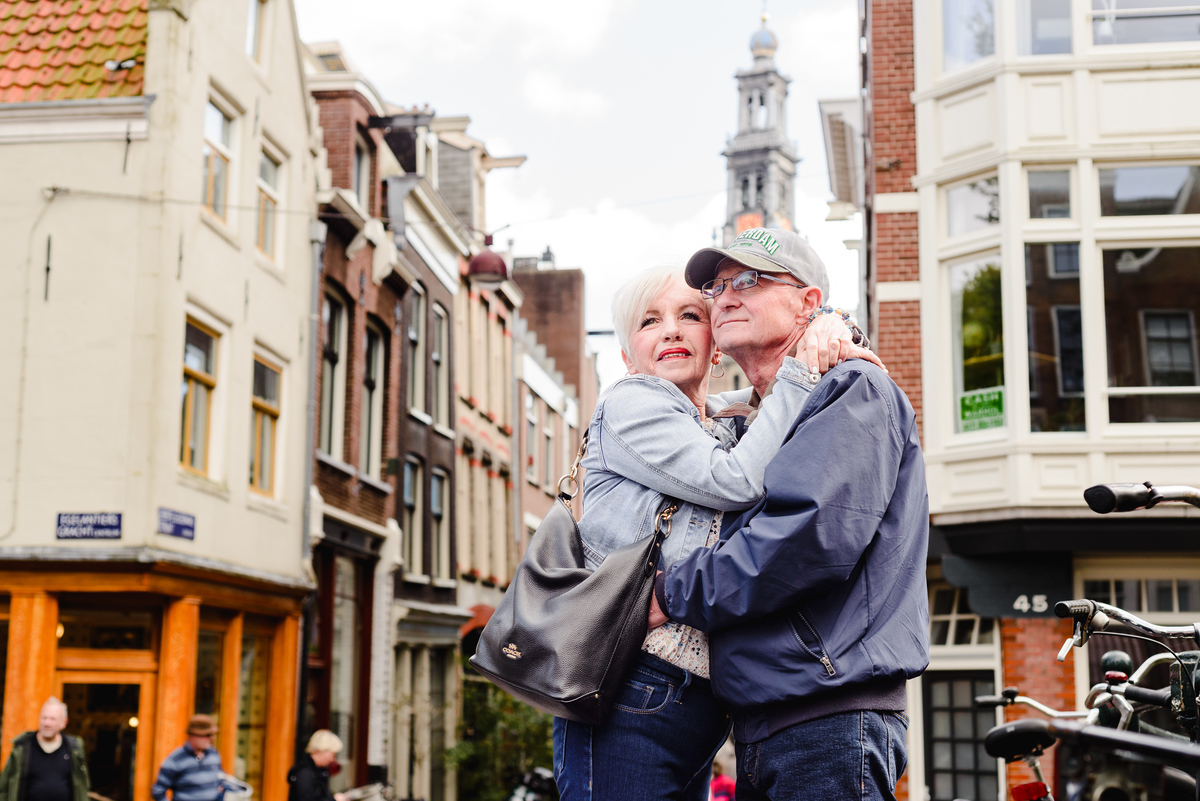 Romantic close-up of an anniversary couple holding each other in a quiet Amsterdam street with historic buildings behind them.