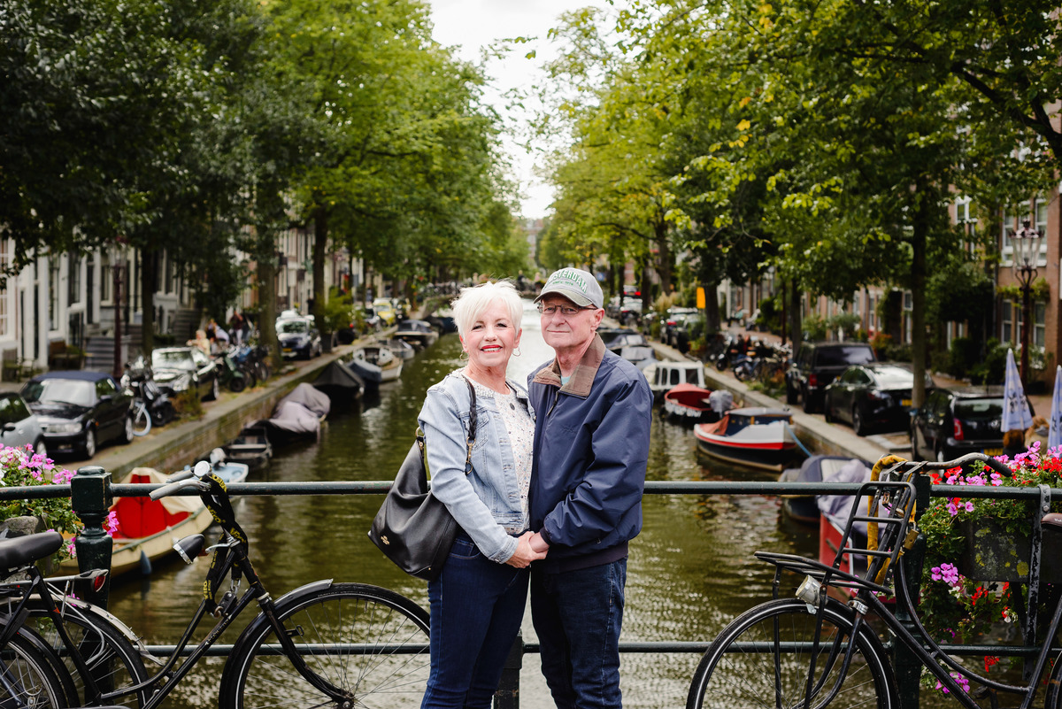 Portrait of a couple smiling at the camera on a canal bridge, Amsterdam canal stretching behind them.