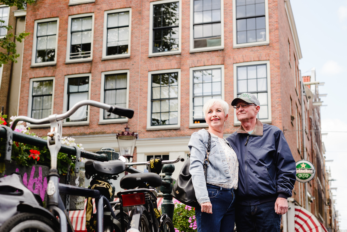 Couple standing near parked bicycles with a brick canal house behind them, relaxed and casual moment.