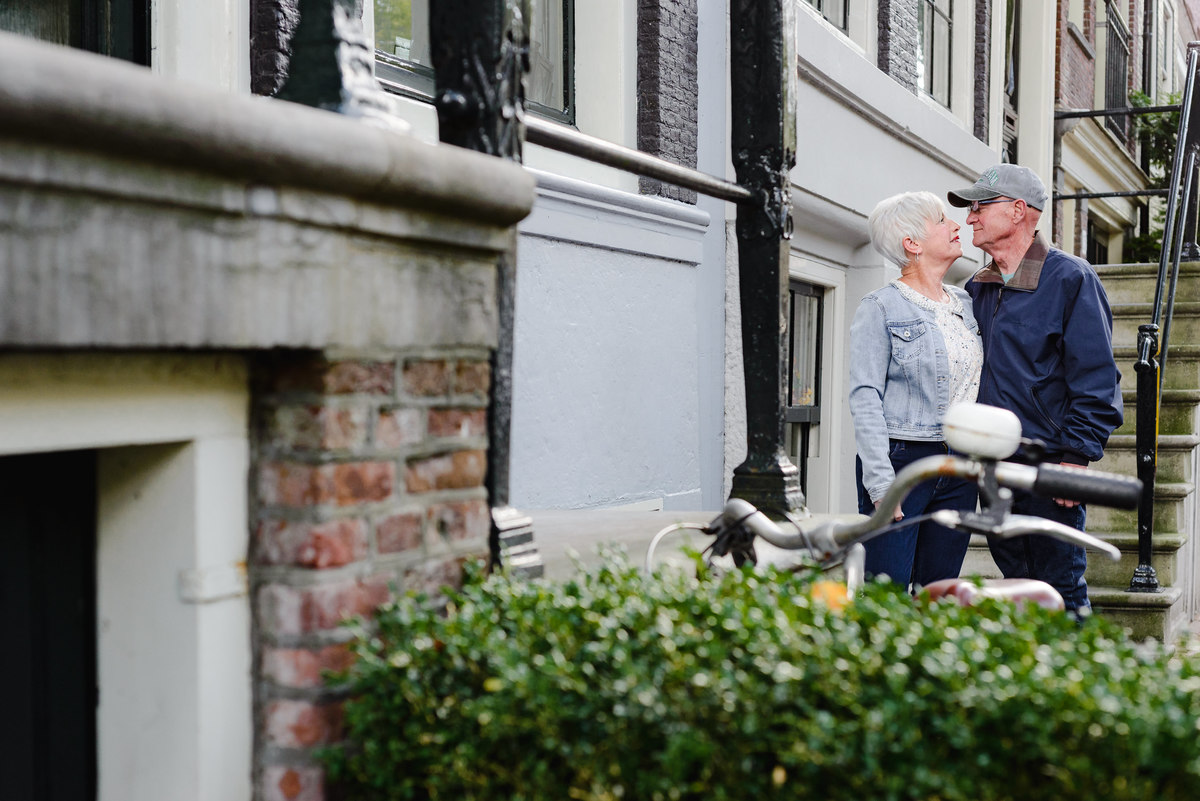 Couple leaning in close beside a canal house facade, intimate moment on a quiet Amsterdam street.