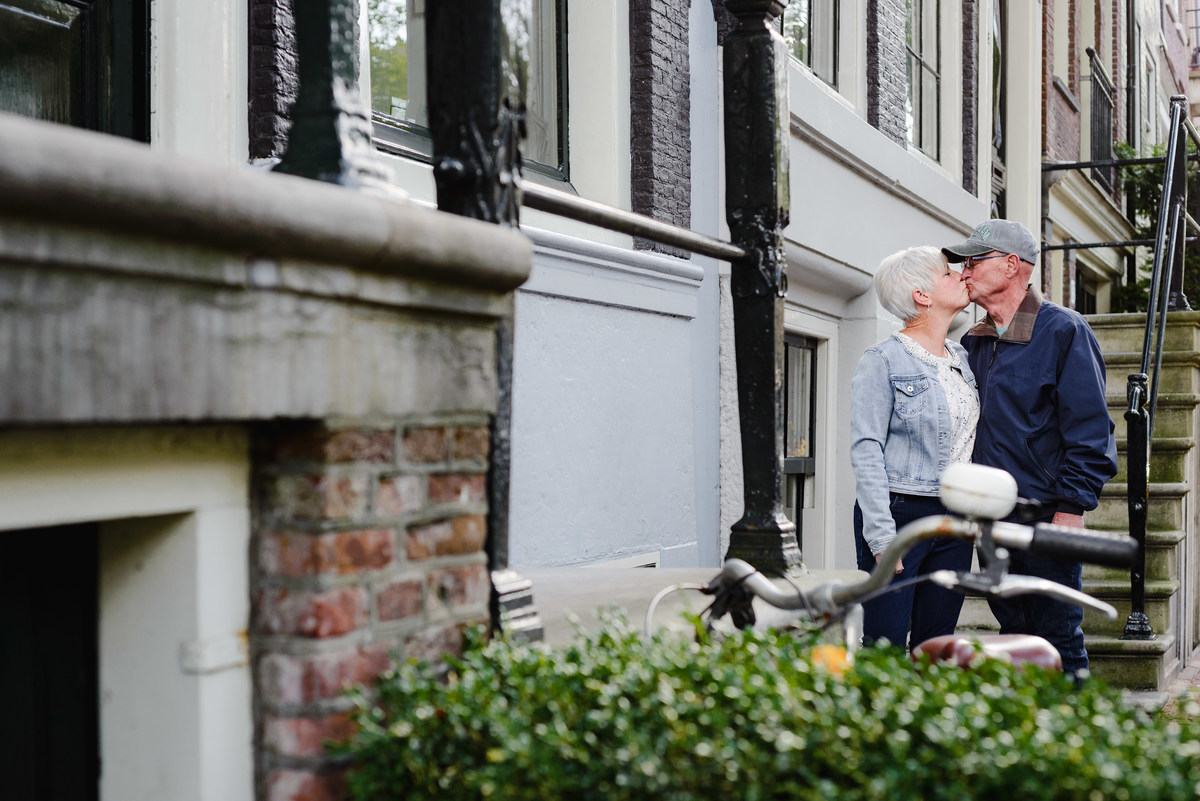 Couple kissing softly near the steps of a canal house, bicycles partially visible in the foreground.
